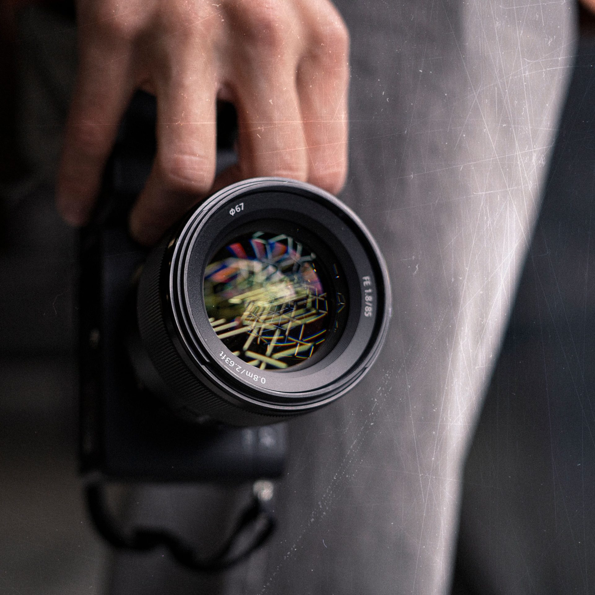 A detailed view of a lens being held, showcasing reflection details and artistic scratches.