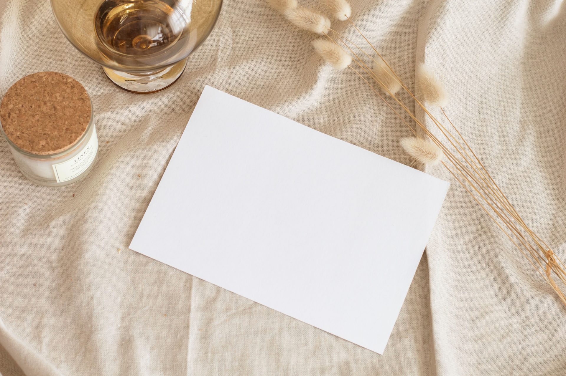 A serene still life featuring a blank paper, scented candle, and dried grass on linen.